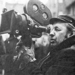 Czarno-biała fotografia przedstawiająca Andrzeja wajdę z kamerą filmową
