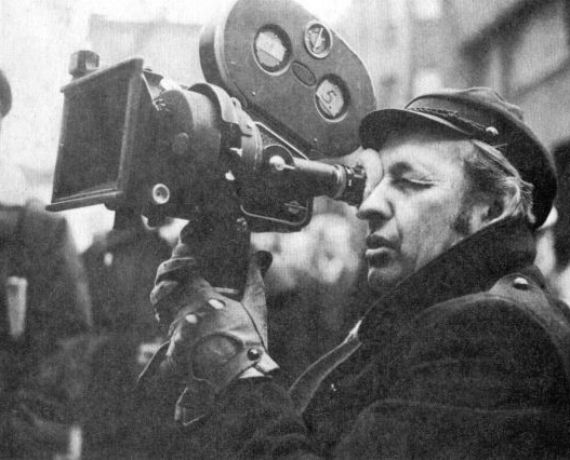 Czarno-biała fotografia przedstawiająca Andrzeja wajdę z kamerą filmową